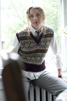 a woman sitting on top of a radiator wearing a sweater vest and tie