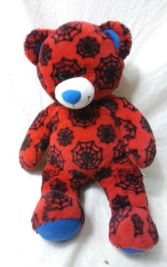 a red and black teddy bear sitting on top of a white bed sheet with spider webs all over it