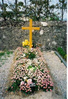 a yellow cross sitting on top of a lush green field next to a stone wall