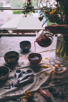 a person pouring tea into small bowls on a table with flowers and spoons next to them