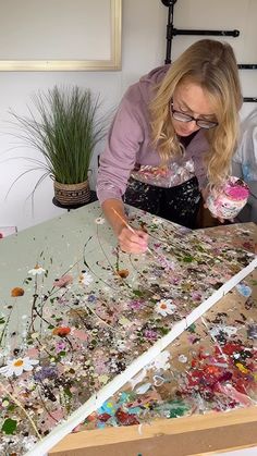 a woman is working on an art project with paint and flowers in front of her