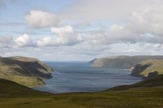 the ocean is surrounded by hills and grass on both sides, with white clouds in the sky