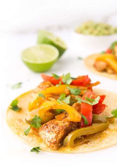 two tacos with chicken, peppers and cilantro on them next to limes