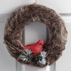 a red bird sitting on top of a wreath hanging from the front door with pine cones