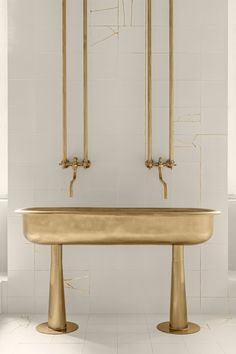 a large gold bathtub in a white tiled bathroom with two tall brass fixtures on the wall