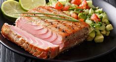 a black plate topped with meat next to a salad and lime wedges on top of a wooden table