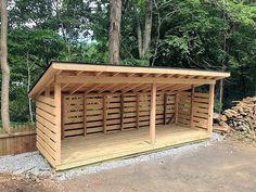 a wooden shelter in the middle of a wooded area with lots of wood stacked around it