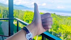 a person giving the thumbs up sign on a balcony overlooking trees and mountains in the distance