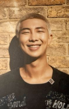 a young man smiling in front of a brick wall