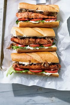 three sub sandwiches sitting on top of a white paper wrapper next to each other