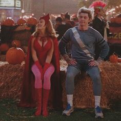 a man and woman dressed up in costumes sitting on hay bales with pumpkins behind them