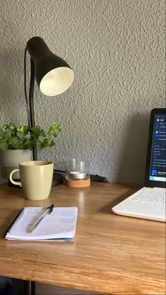 an open laptop computer sitting on top of a wooden desk next to a cup of coffee