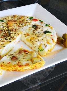 a white plate topped with an omelet covered in cheese next to olives