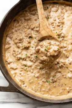 a wooden spoon in a skillet filled with meat and gravy