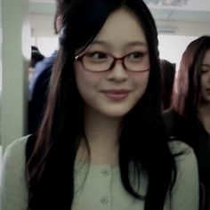 a woman with long black hair and red glasses is standing in front of other people