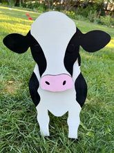 a black and white cow is standing in the grass