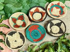 four woven baskets sitting on top of a table next to green plants and leaves in the background