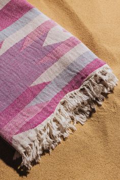 a pink and white blanket laying on top of a sandy beach