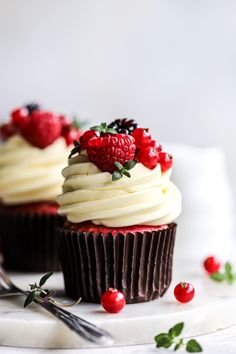 two cupcakes with white frosting and raspberries are on a plate