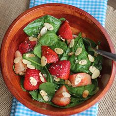 a bowl filled with spinach and strawberries on top of a blue checkered table cloth