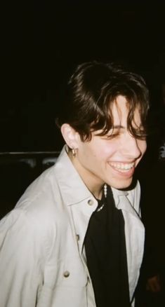 a young man wearing a white shirt and black tie smiles at the camera while standing in front of a dark background