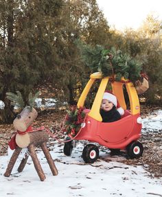 a small child in a red car pulling a reindeer on a sleigh through the snow