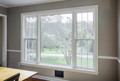 an empty room with two windows and a table in the corner on the far side