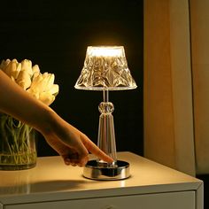 a person reaching for a flower in a vase on a table next to a lamp