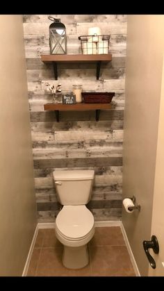 a white toilet sitting inside of a bathroom next to a shelf filled with candles and other items