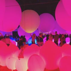 many people are standing around in the dark with pink lights on them and white balls hanging from the ceiling