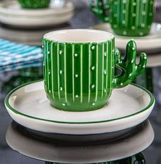 a green coffee cup sitting on top of a white plate next to a cactus plant