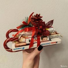 a person holding up a box filled with chocolates and candy bar wrapped in red ribbon