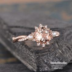 an engagement ring with a pink diamond and pearl accents on top of a piece of wood