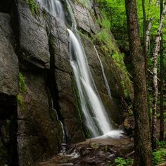 there is a waterfall in the middle of some trees and rocks with water running down it