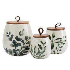 three ceramic containers with wooden lids and leaves painted on them