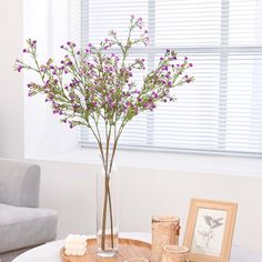 a vase with purple flowers sitting on top of a white table next to a gray couch