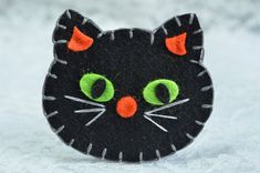 a black cat brooch with green eyes and orange ears sitting on snow covered ground