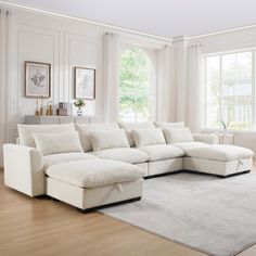 a large white sectional couch in a living room with hardwood flooring and two windows