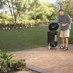 a man standing next to a black bbq on top of a brick floor in a yard