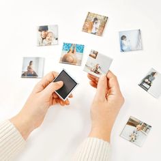 a person holding a cell phone in front of many polaroid pictures on a table