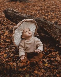 a baby sitting on the ground with an umbrella over its head and leaves around it