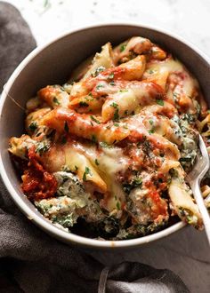 a white bowl filled with pasta and spinach on top of a gray cloth next to a spoon