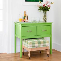 a green table with flowers and drinks on it in front of a white wall, next to a stool