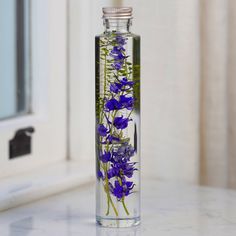 a glass bottle filled with purple flowers sitting on top of a marble counter next to a window