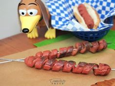 two hot dogs on skewers next to a paper basket with fake sausages