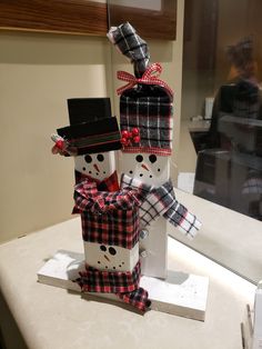 two snowmen wearing hats and scarfs are standing next to each other on a table