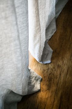 a bed with white sheets and wooden flooring next to a window covered in curtains