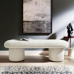 a white bench sitting on top of a wooden floor next to a rug and painting