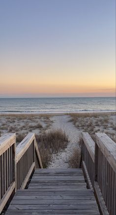 a wooden walkway leading to the beach at sunset