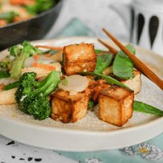 tofu and broccoli on a plate with chopsticks next to it